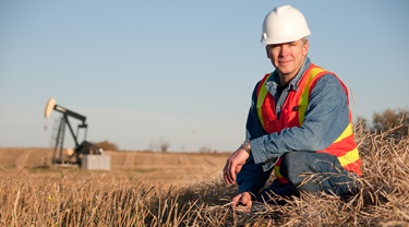 Albertan engineer in safety gear inspects soil near oil well pumpjack