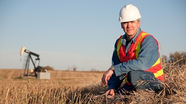 Albertan engineer in safety gear inspects soil near oil well pumpjack