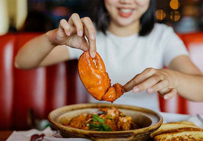 A woman holds a Canadian lobster claw above her hot pot.