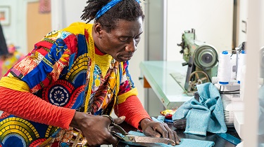 Un designer portant une veste multicolore coupe du tissu pour faire un vêtement