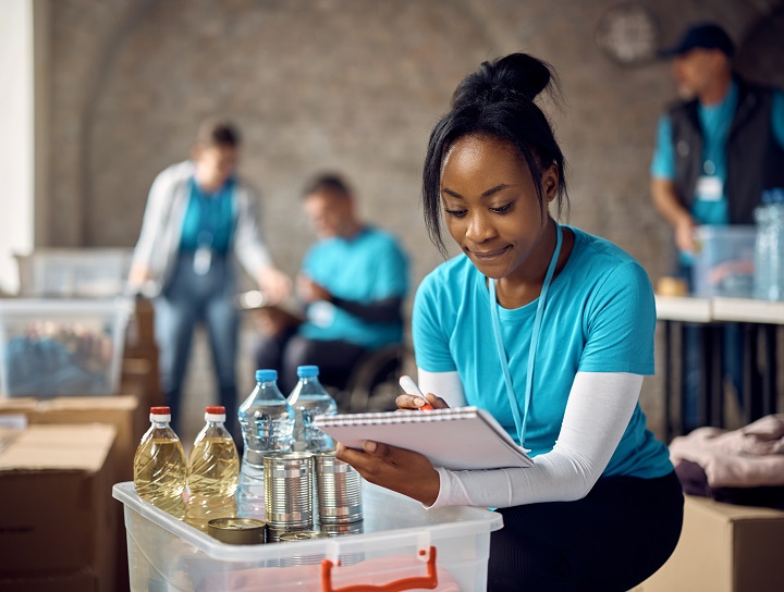 Une femme noire travaillant bénévolement dans une banque alimentaire calcule les dons.