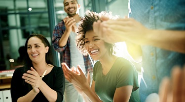 Work colleagues (men and women) smile and clap their hands to celebrate their company’s success.