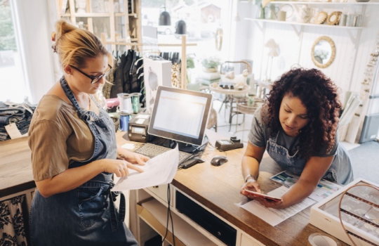 Deux collègues féminines discutant de reçus financiers avec une tablette numérique à la caisse d'un magasin.