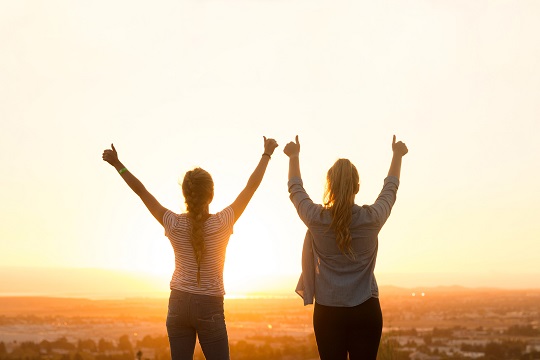Two young women giving a thumb’s up to the sky