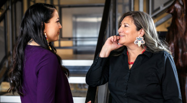 Two Indigenous women have a conversation in an office lobby. 