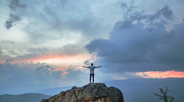 Man standing on top of a mountain with his arms in the air.