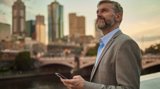 Businessman holding phone at dusk in Melbourne centre city.
