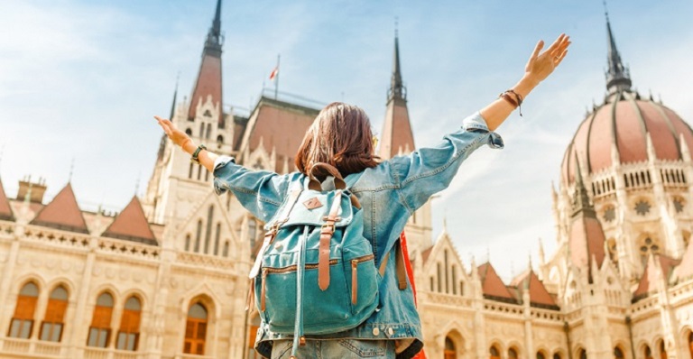 A person wearing a backpack looks up at the Hungarian parliament buildings.