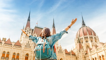 A person wearing a backpack looks up at the Hungarian parliament buildings.