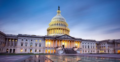 The US Capitol building at dusk, with dramatic lighting highlighting its iconic dome and neoclassical architecture against a clear blue sky.