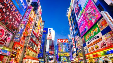 Crowds pass by colourful signs in busy Japanese shopping area.