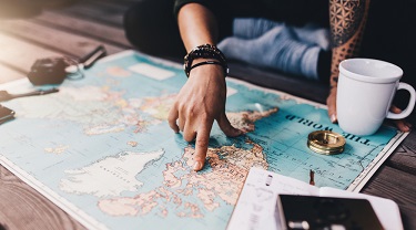 There is a world map on a coffee table. Someone is pointing to North America on the map.