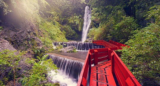 A red pedestrian bridge winds through small waterfalls. The bridge leads to a famous Chilean hot springs spa.