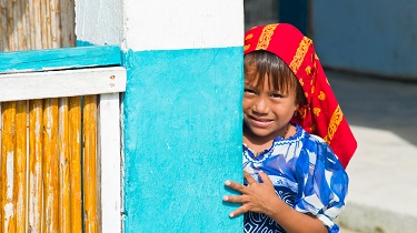 Un enfant portant une coiffe sourit à l’objectif, dissimulé derrière une porte.