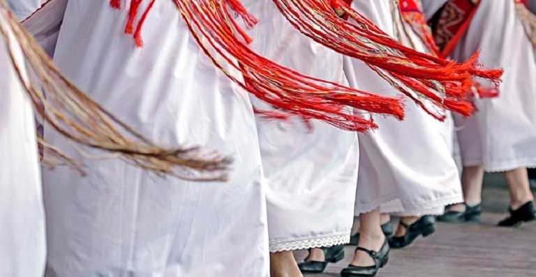 A line of dancers are seen from the waist down wearing traditional clothing.