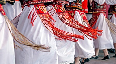 A line of dancers are seen from the waist down wearing traditional clothing.
