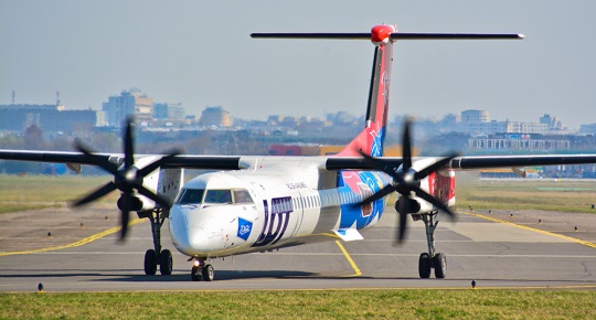 A small plane moves down a runway with a city in the far background.