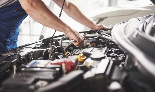 Les bras d’un homme plongent dans le moteur d’une voiture.