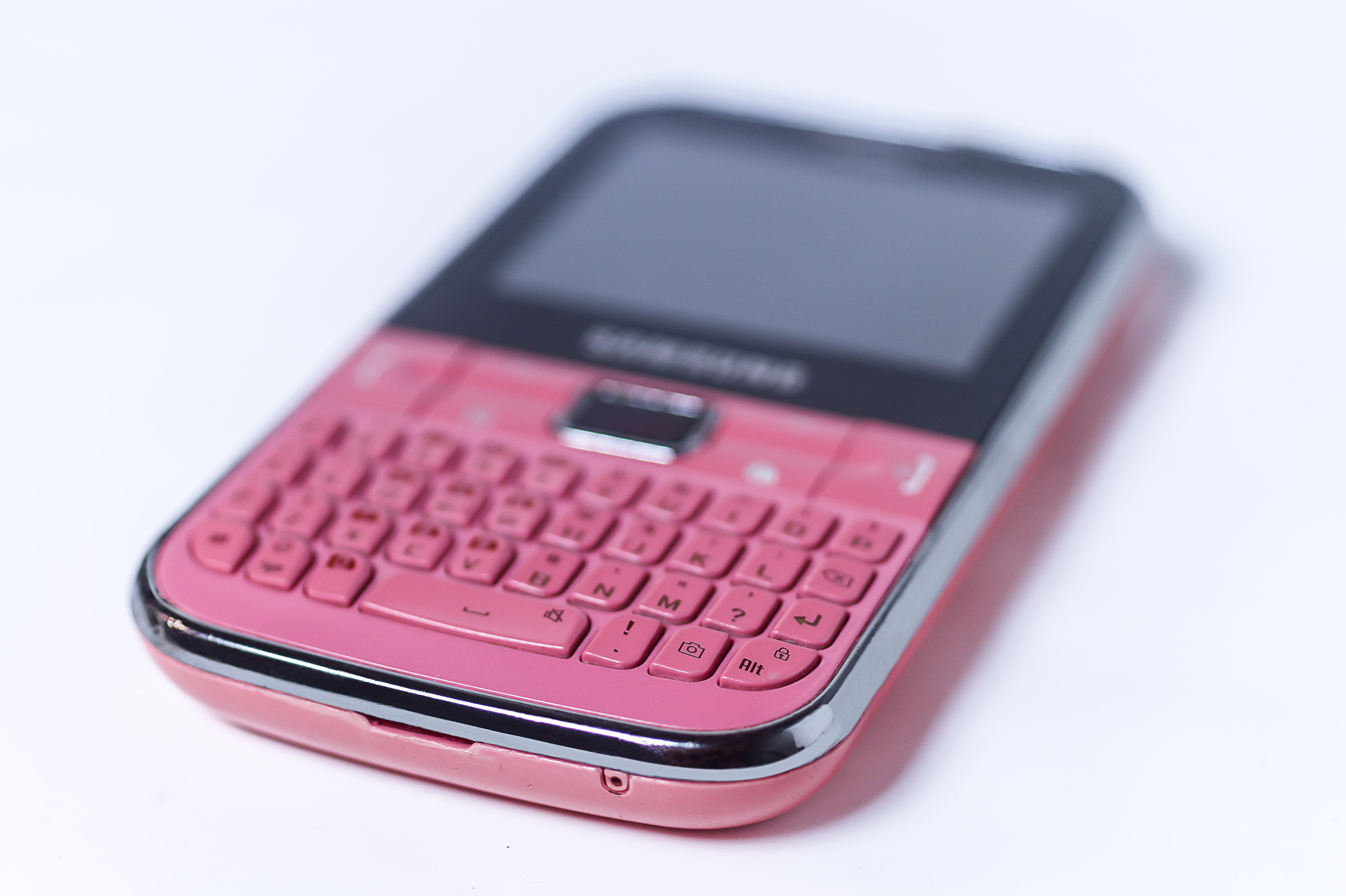 Un téléphone portable rose vintage doté d'un clavier physique, posé sur une surface blanche.