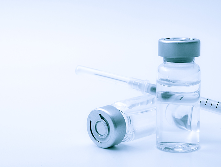 Des flacons médicaux en verre et une seringue posée sur une surface blanche.