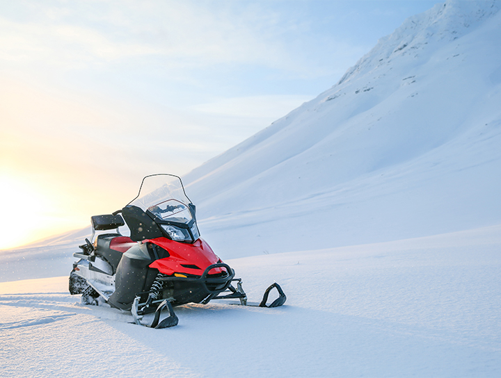 Une motoneige rouge garée dans un paysage enneigé au lever du soleil.