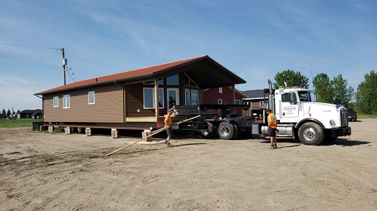 Un camion à plateau livrant des maisons usinées de SK2 en un seul morceau.