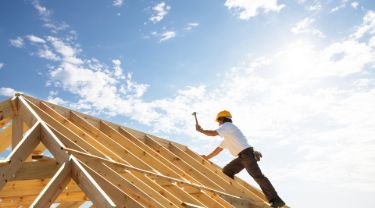 Man building a roof with fluffy clouds in the background.