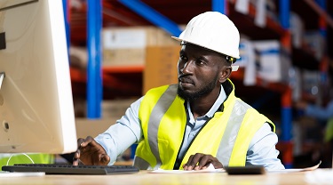 Worker on a computer in a warehouse preparing goods to ship.