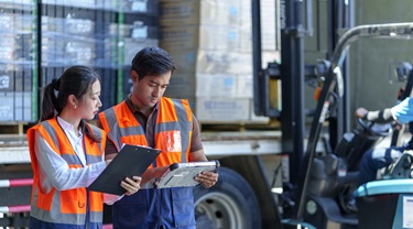 Les employés d'entrepôt vérifient les documents pendant que le chariot élévateur charge l'expédition dans un camion.