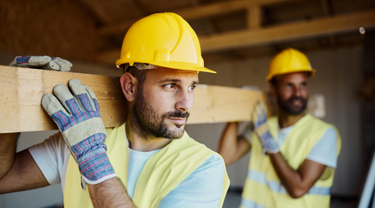 Construction workers carry wooden beam on site.