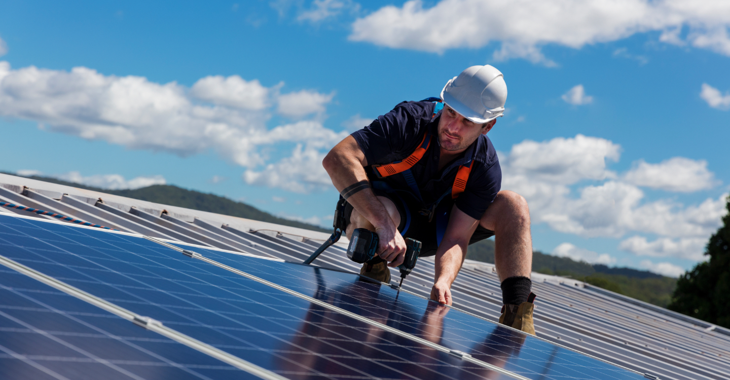 Homme portant un casque de protection et un pantalon court qui installe des panneaux solaires