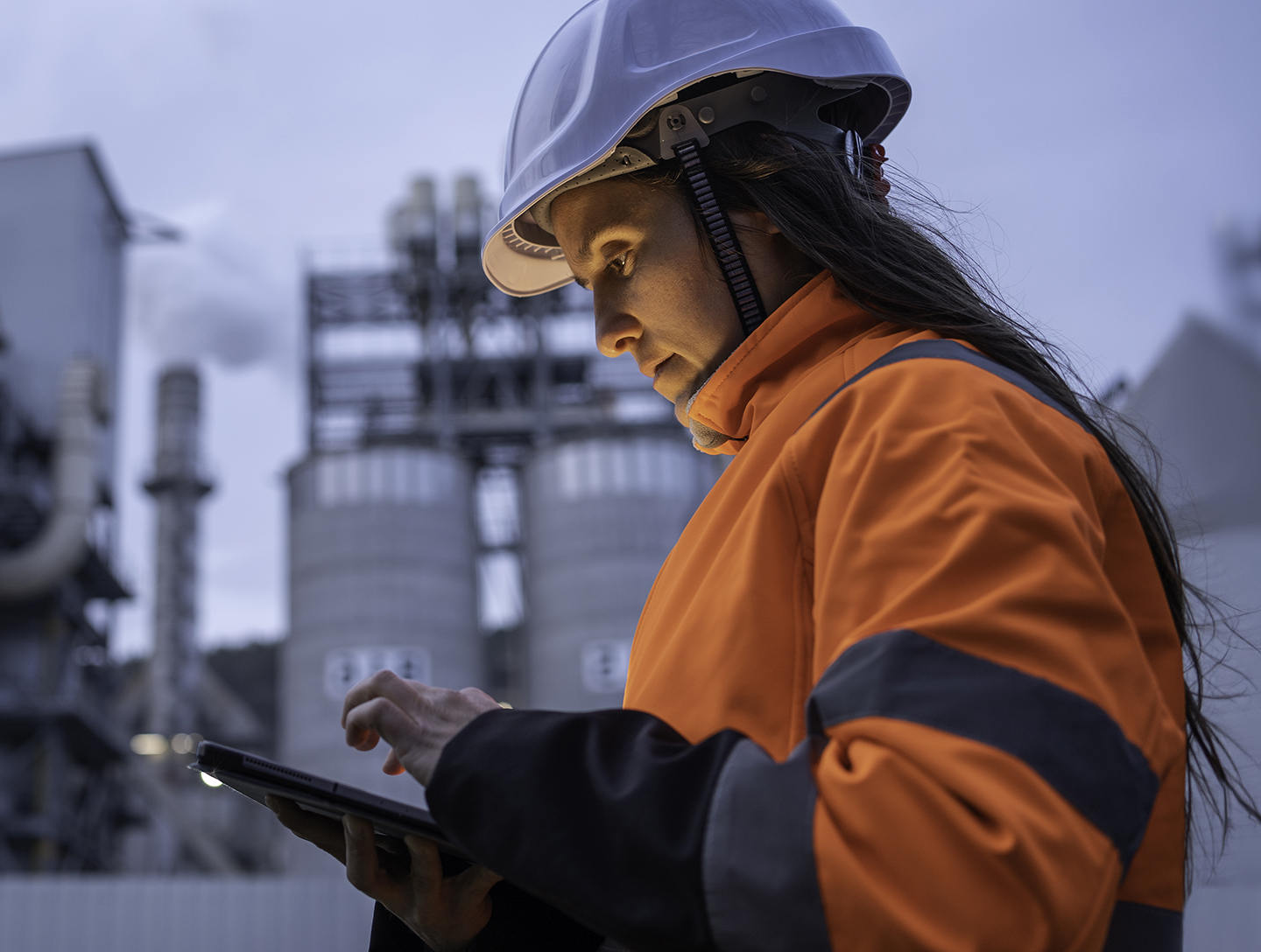 Personne portant un casque de sécurité et utilisant une tablette dans une installation industrielle pour consulter des informations sur les activités et la chaîne d’approvisionnement.