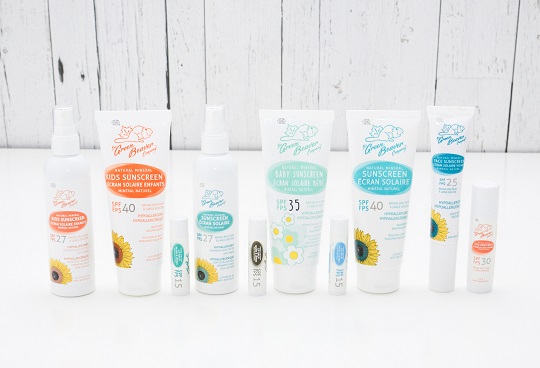 A selection of Green Beaver sunscreen products sit lined up on a white surface with a background of white wood panels.