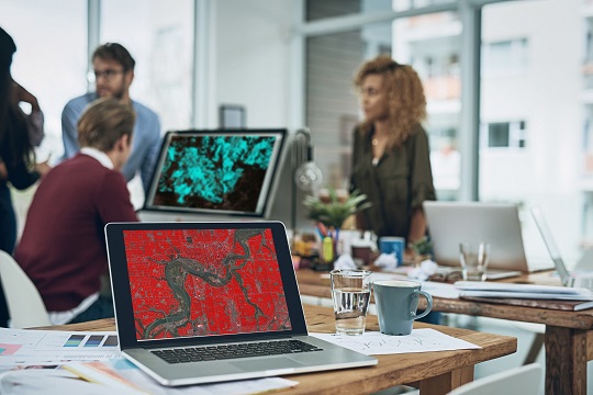 Posé sur un bureau, un ordinateur portable affiche une carte rouge vif.