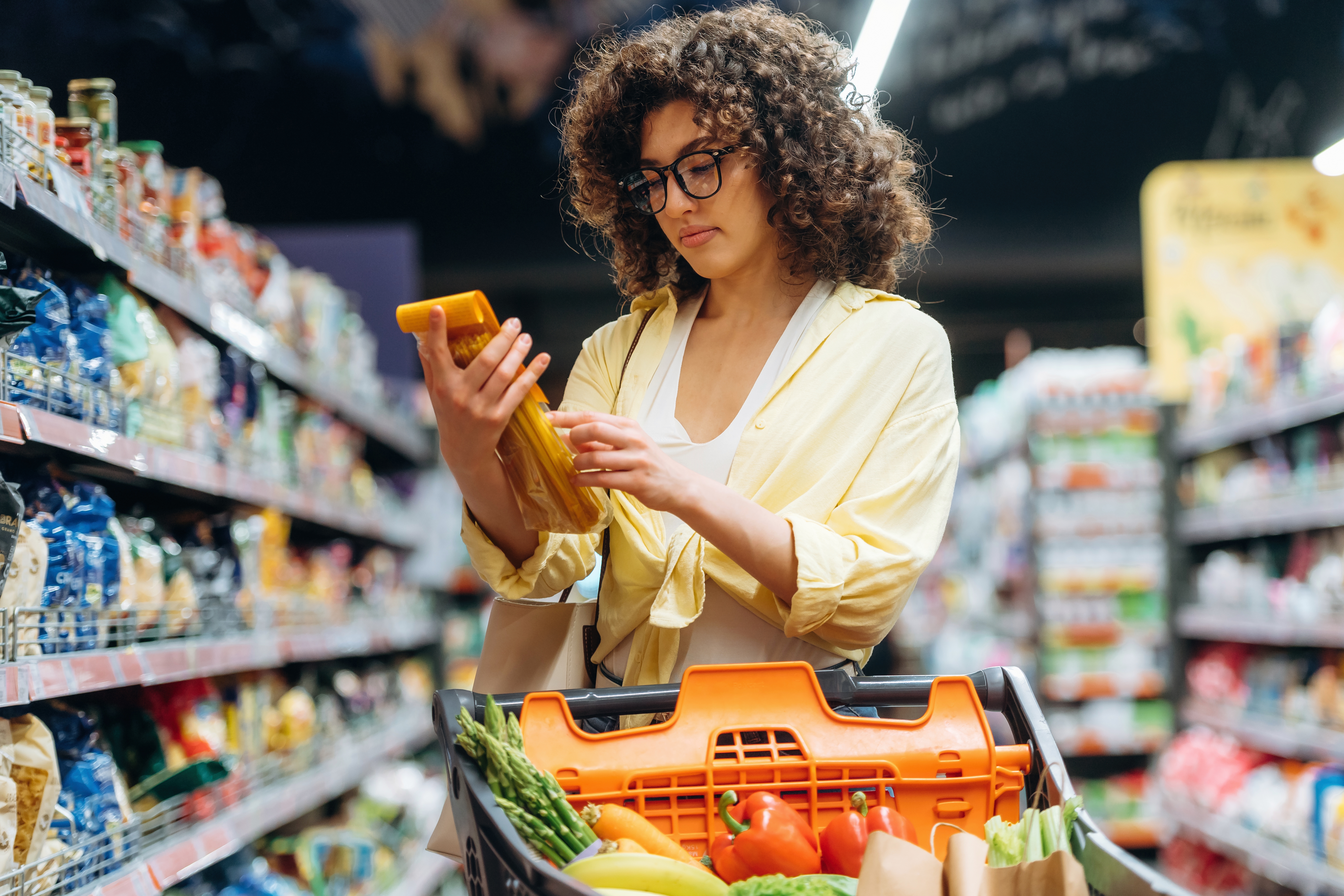 Une femme pousse un panier d’épicerie contenant des fruits et des légumes frais