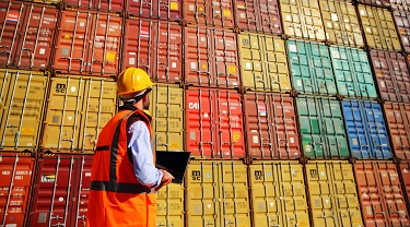 Warehouse worker taking inventory of stacked cargo containers.