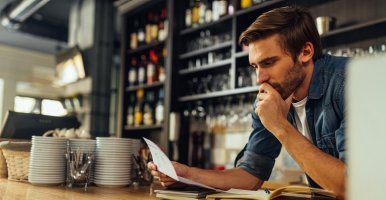 Worried restaurant owner checks business documents while standing behind counter