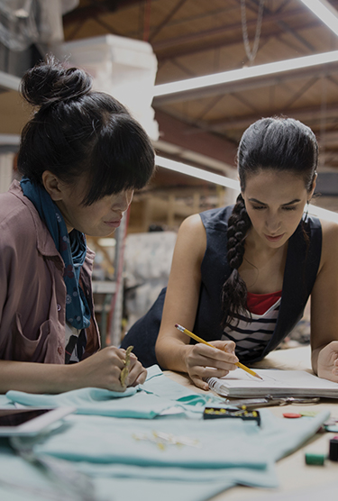 Female designers brainstorming and sketching at a workbench in a workshop