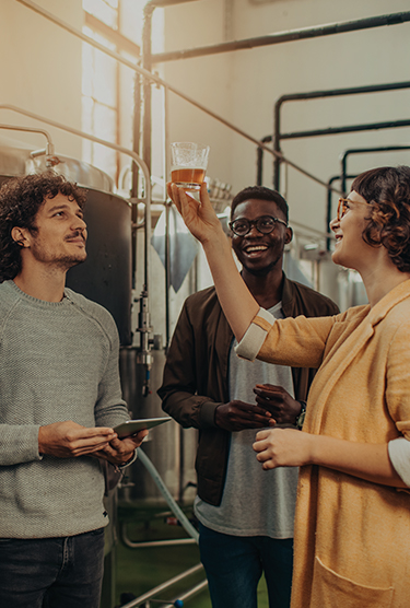 Three employees at a craft brewery examining a sample of beer in a glass