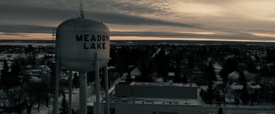 A white water tower that says ‘Meadow Lake’ with the town in the background as the sun rises.