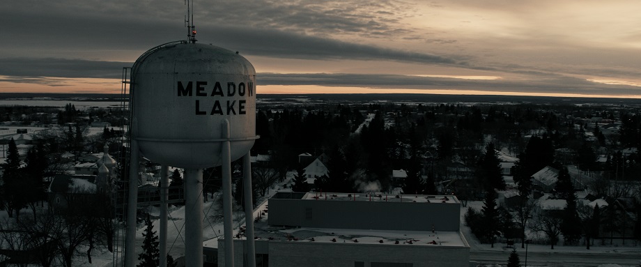 Un château d'eau blanc qui dit "Meadow Lake" avec la ville en arrière-plan lorsque le soleil se lève.