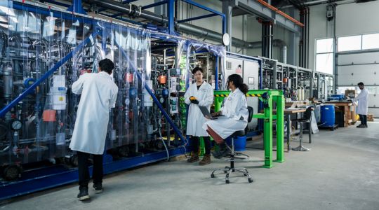 Des travailleurs portant un sarrau se tiennent devant l’équipement électrochimique de Mangrove Lithium, qui est utilisé pour le raffinage du lithium.