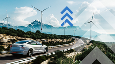 An electric car on a highway with wind turbines and mountains in the distance.