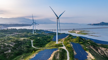 Éoliennes et panneaux solaires photovoltaïques au coucher du soleil en bordure de l’océan.