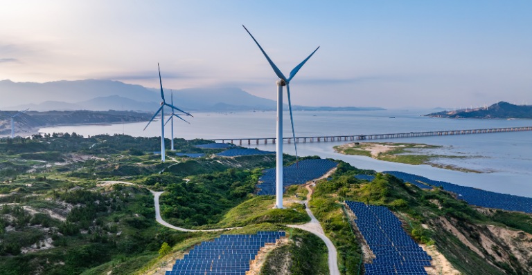 Éoliennes et panneaux solaires photovoltaïques au coucher du soleil en bordure de l’océan.