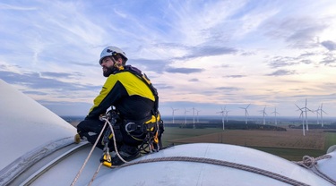 Technicien d’éolienne allemand sécurisé sur la nacelle, dominant un vaste parc éolien sous ciel nuageux