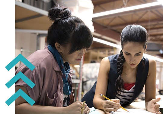 Female designers brainstorming and sketching at a workbench in a workshop