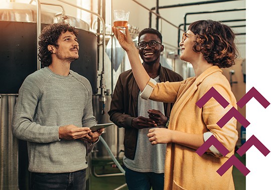 Three employees at a craft brewery examining a sample of beer in a glass