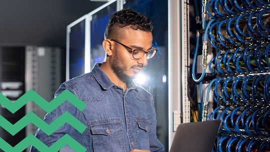 Man in denim shirt checking laptop at wall of blue hoses 