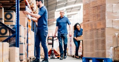 Three warehouse workers move packages onto pallets.